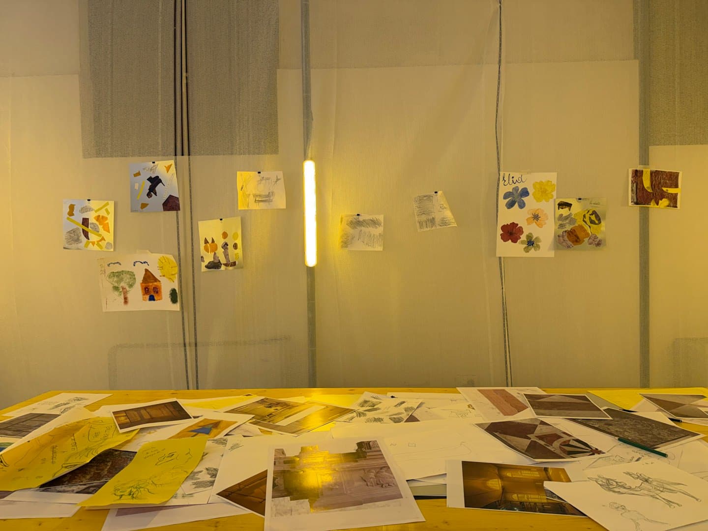 Kreativer Arbeitsplatz mit Kunstbedarf auf einem Holztisch und bunten Zeichnungen an der Wand.