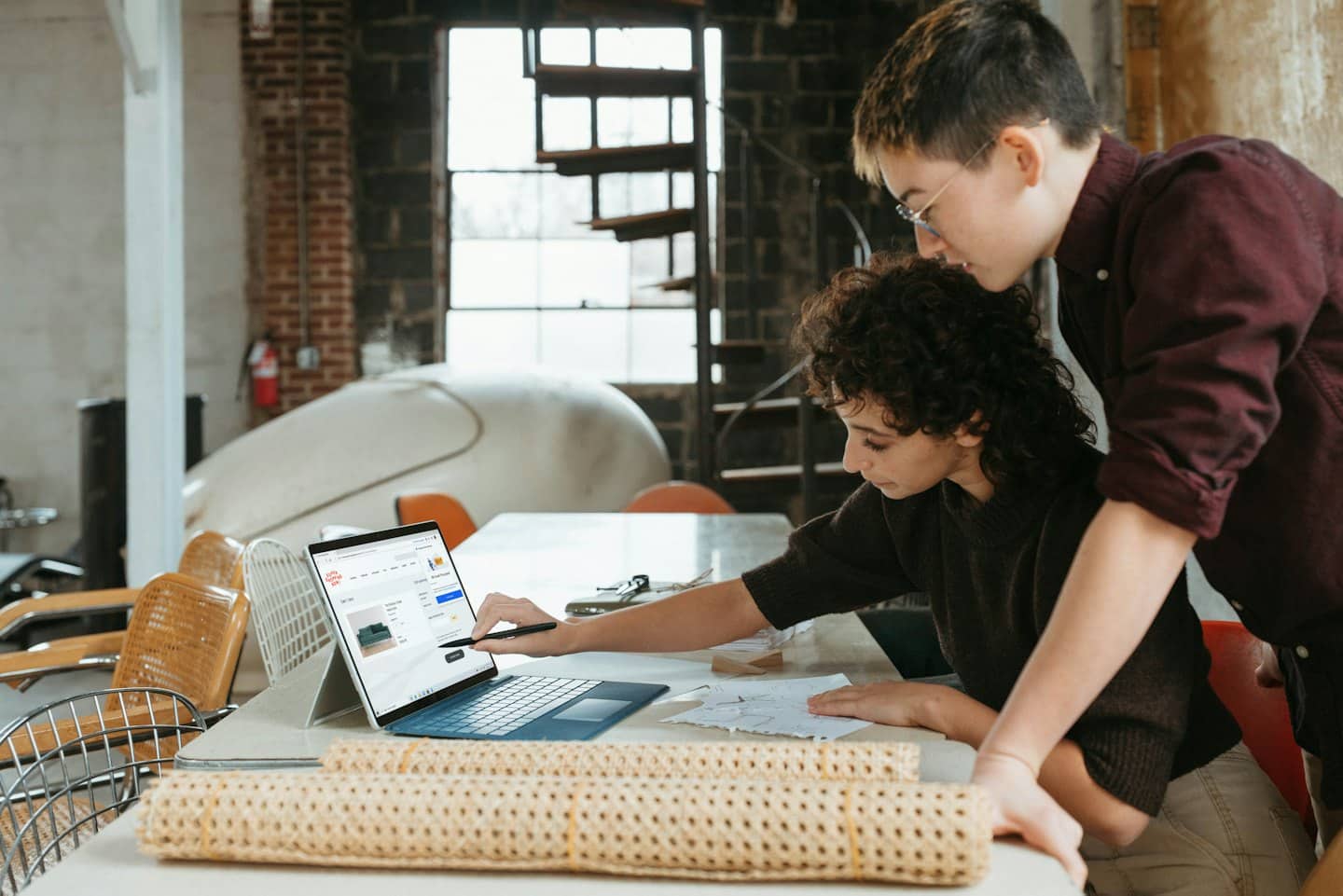 Zwei Designer arbeiten gemeinsam an einem Laptop mit Produktbildern auf dem Bildschirm.