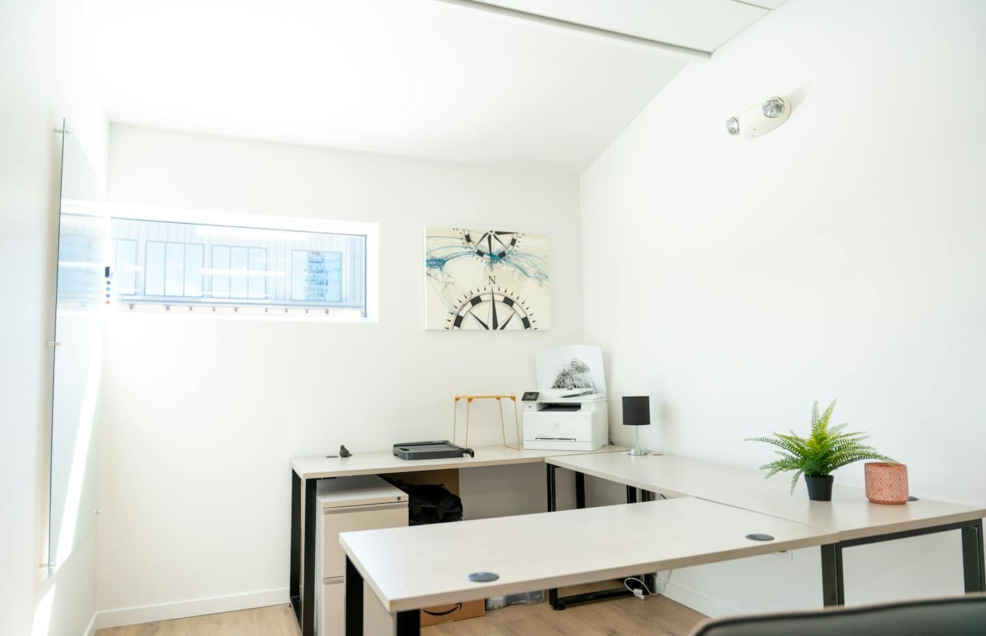 Minimalistisches Heimbüro mit L-förmigem Schreibtisch und Kompass-Kunstwerk.